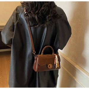 Brown vintage flap bag shown crossbody on model with wooden bead charm and metal lock