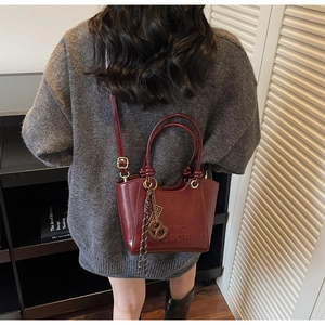 Détail d'un sac seau bordeaux avec texte DEOR en relief et pendentif pompon décoratif