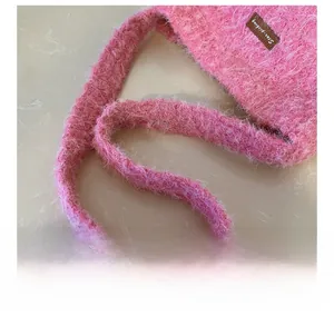 Close-up of pink plush bucket bag with brown leather brand tag and soft shoulder strap