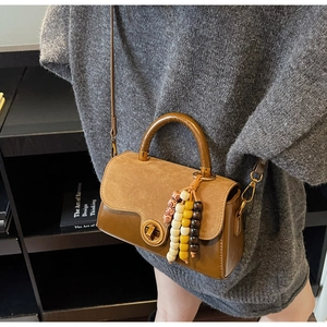 Detail view of a vintage brown leather crossbody bag with a round lock and beaded charm