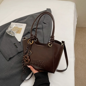Détail d'un sac seau en cuir brillant marron foncé avec logo embossé et anneaux dorés