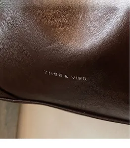 Detail view of dark brown leather bucket bag showing fine texture and silver logo engraving
