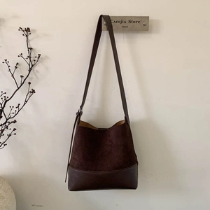 Detail of dark brown suede bucket bag featuring adjustable leather strap and smooth base
