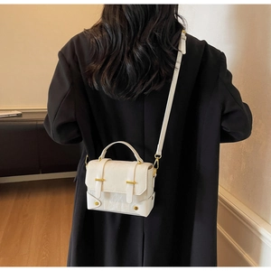 Petit sac messager blanc minimaliste avec détails dorés porté par un mannequin