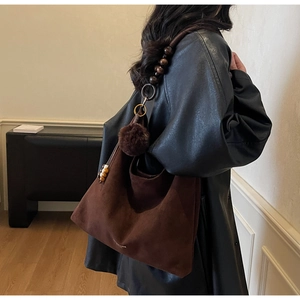 Détail du sac fourre-tout en daim marron avec perles en bois sur la bandoulière et pompon