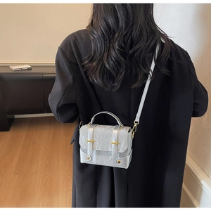 Vue détaillée du sac messager gris plissé avec boucle dorée sur un blazer noir
