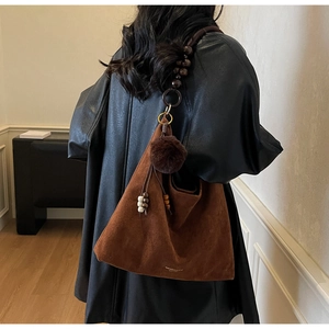 Détail du sac hobo en daim marron avec bandoulière en perles et pompon en peluche