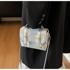 Détail d'un sac messager en cuir argenté froissé avec boucles dorées et poignée haute