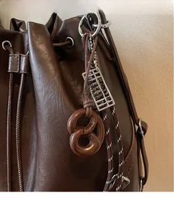 Detail of dark brown drawstring bucket bag with pretzel and silver abacus charms