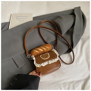 Detail of a brown mini crossbody bag featuring white lace trim and a plush baguette charm
