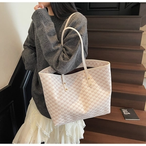 Detail of the beige tote bag with NK pattern, long leather straps and gold rivets