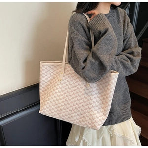 Detail of cream tote bag with monogram print and gold rivets worn on shoulder