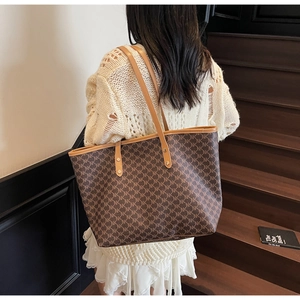 Detail of dark brown NK monogram tote bag with leather straps on a female model