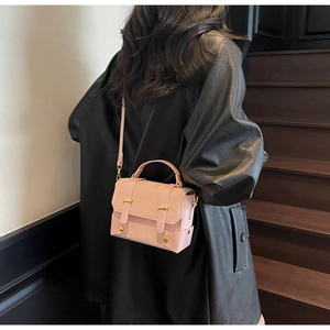Détail du mini sac messager rose structuré avec boucles dorées sur tenue en cuir noir
