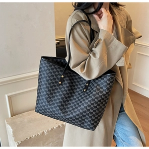 Detail of NK monogram canvas tote bag showing black leather straps and gold rivets