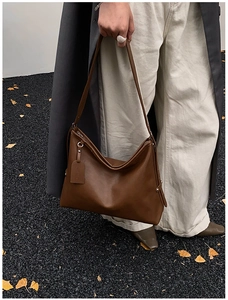 Detail of a brown leather tote bag with a matching tag held by a model on a street
