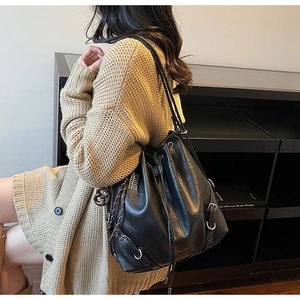 Detail of black drawstring bucket bag with silver buckle and braided rope charm accessory