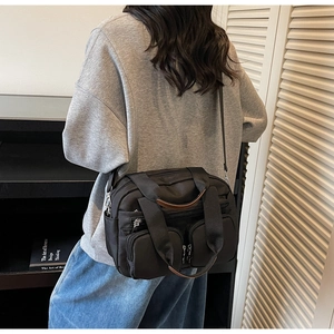 Detail of black utility shoulder bag with dual zipper pockets and brown leather handle