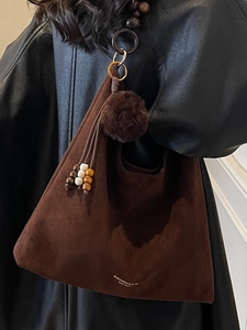 Sac cabas vintage en daim marron avec pompon décoratif et glands, porté comme un sac à bandoulière