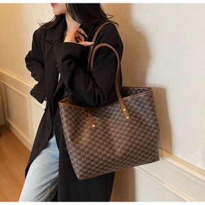 Detail of a large brown MK monogram tote bag featuring gold rivets and leather handles