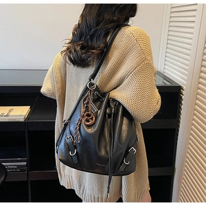 Detail of a black bucket bag with silver buckle, brand logo, and woven charm on a model