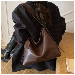 Detail of dark brown leather tote bag showing wide strap and metallic protective studs