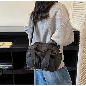 Detail of black nylon tote bag with dual front zipper pockets and brown leather trim