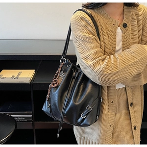 Detail of black drawstring bucket bag with side metal buckle and woven charm accent