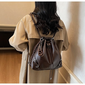 Detail of dark brown drawstring bucket bag featuring sleek leather texture and metal buckle