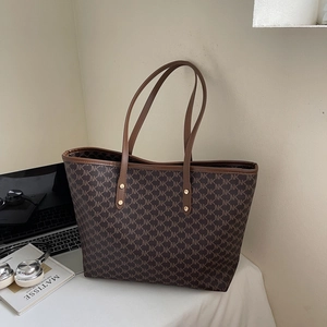 Close-up of brown tote bag with NK pattern, leather straps and gold rivets in a lifestyle setup