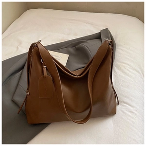 Detail of a brown leather tote bag with Korea Bags tag on a grey blazer suit jacket