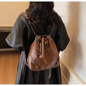 Detail view of retro brown leather drawstring bucket bag worn over a black leather coat