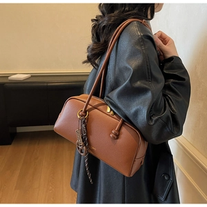 Close-up of brown pebbled leather shoulder bag with gold zipper and woven charm detail