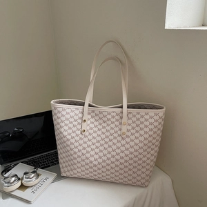 Close-up of beige tote bag with monogram pattern and golden metal rivet details