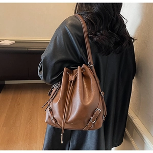 Detail of a brown leather drawstring bucket bag with buckle and woven charm on a model