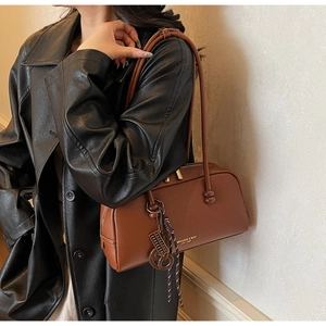 Detail of caramel pebbled leather bag with gold logo and stylish braided pendant