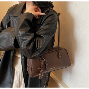 Close-up of a vintage dark brown lychee leather pillow bag with logo print and woven pendant