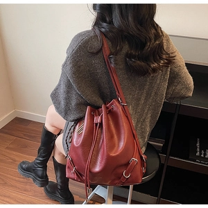 Detail of burgundy bucket bag with drawstring closure shown on model in indoor setting