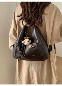 Detail of dark brown PU leather tote bag with gold logo and plush bear charm decoration