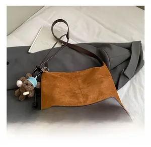 Detail of suede and leather shoulder bag with a cute bear pendant on a neutral bed background