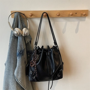 Chic black drawstring bucket bag with woven ring charm hanging on a wooden rack