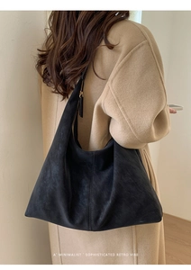 Detail of a black suede tote bag showing the metal zipper and leather pull on a large shoulder bag