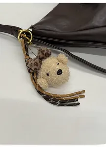 Detail of cute beige plush bear charm with leopard bow on a stylish brown leather tote bag
