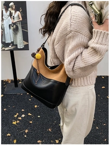Detail view of two-tone bucket bag with yellow pompom charm on autumn ginkgo leaf background
