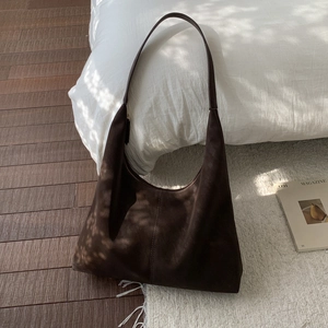 Close-up of a large dark brown suede hobo bag with vertical stitching in a cozy home setting