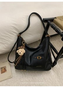 Detail of minimalist black faux leather tote featuring a teddy bear charm and gold buckle
