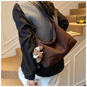 Close-up of brown suede hobo bag with leather corners and cute plush bear accessory