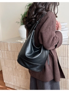 Detail shot of a minimalist black leather tote bag worn by a model in a cozy indoor setting