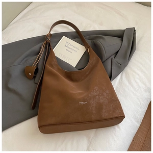 Detail of a brown leather tote bag showing textured suede and heart pendant accessory
