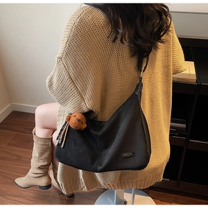 Détail du sac hobo noir mat avec logo métallique carré et pendentif ours en peluche marron